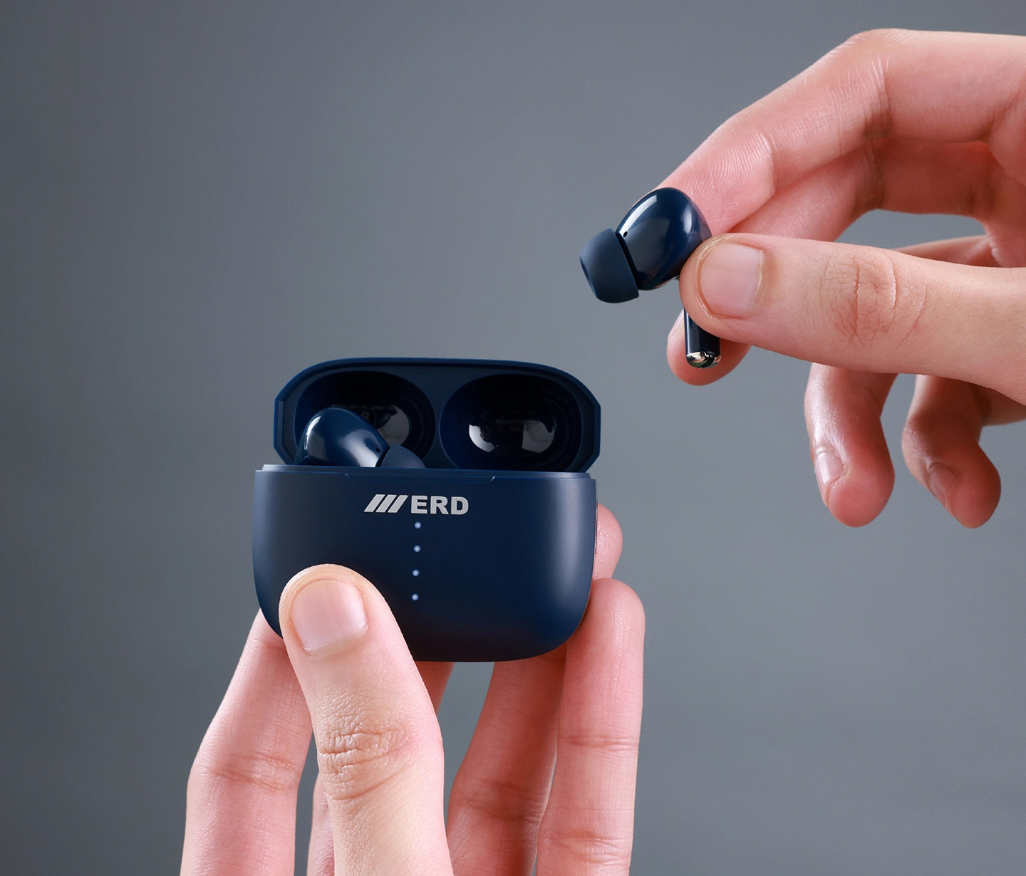 Navy blue wireless earbuds with charging case held by a hand against a gray background