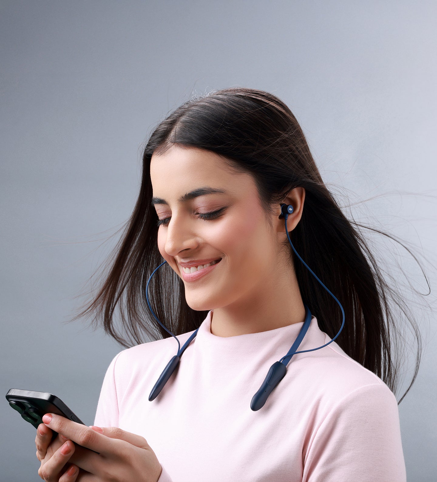 Woman using a smartphone with wireless earbuds against a gray background